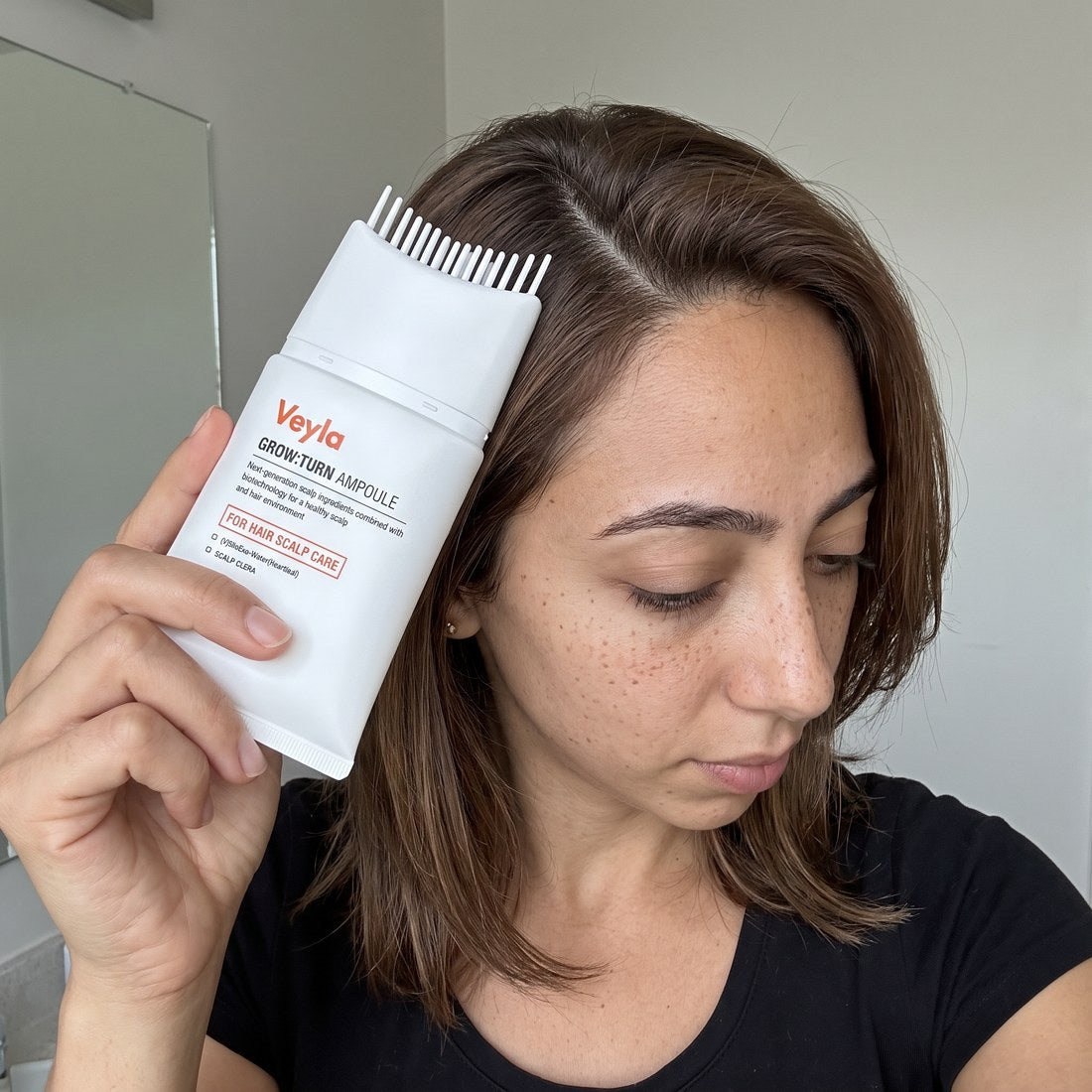 Chloe Mendez combing the serum applicator through her hair at a bathroom mirror
