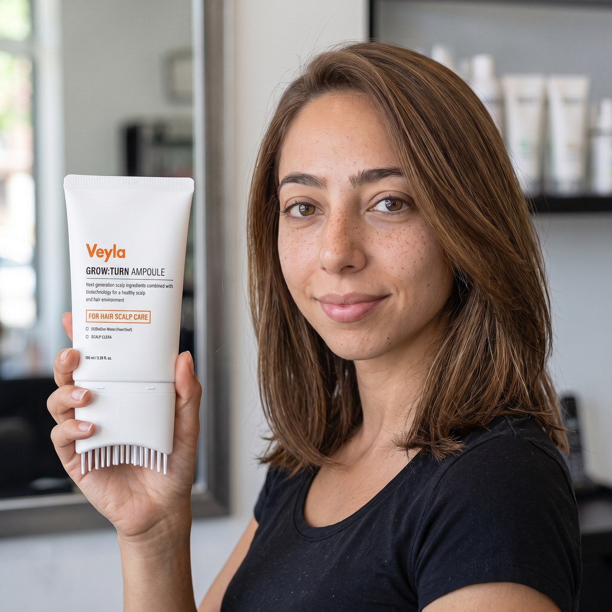 A hairstylist holding the Veyla Grow:Turn Ampoule, showing the label and the comb applicator
