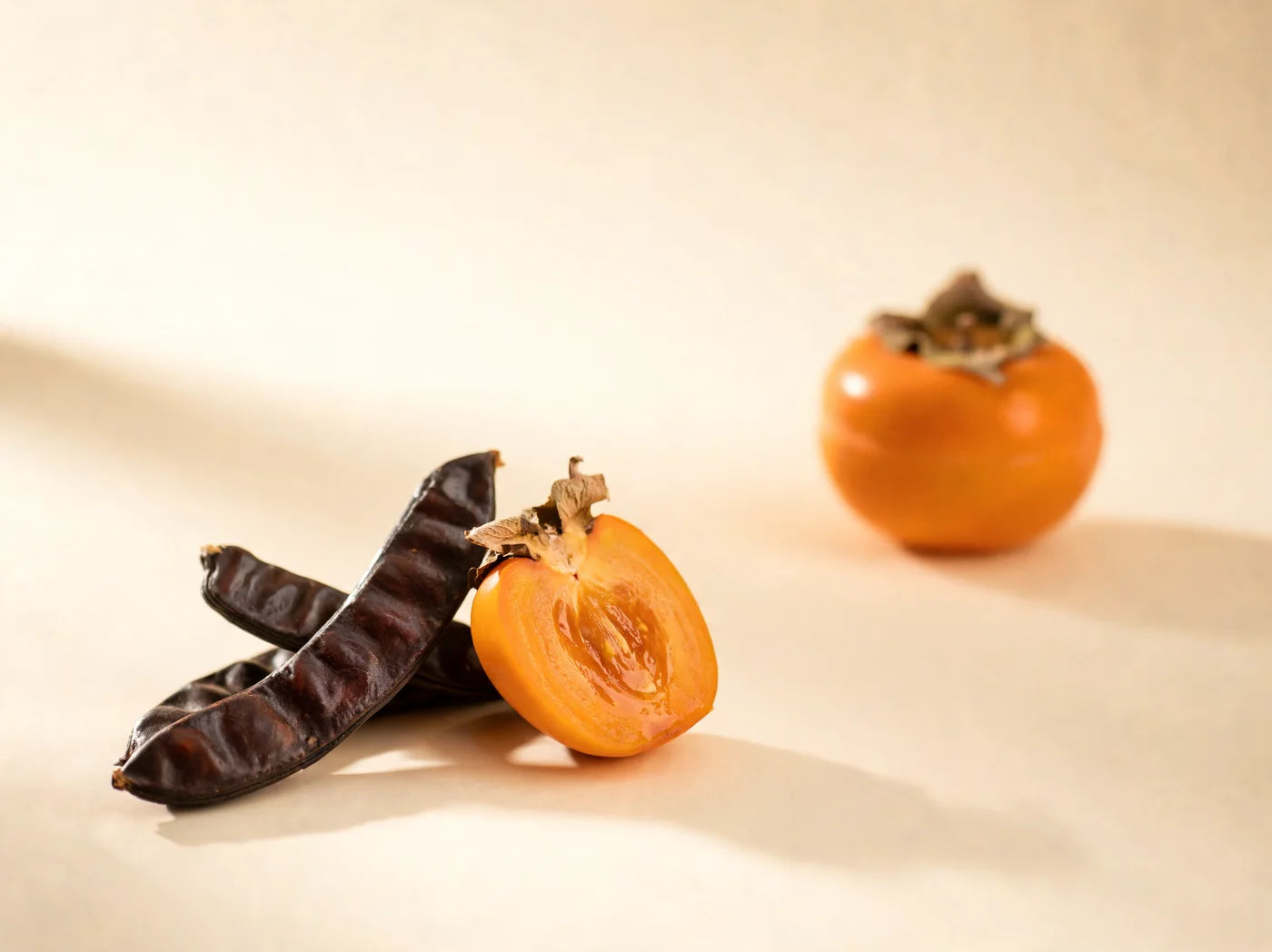 Carob pods beside a halved persimmon