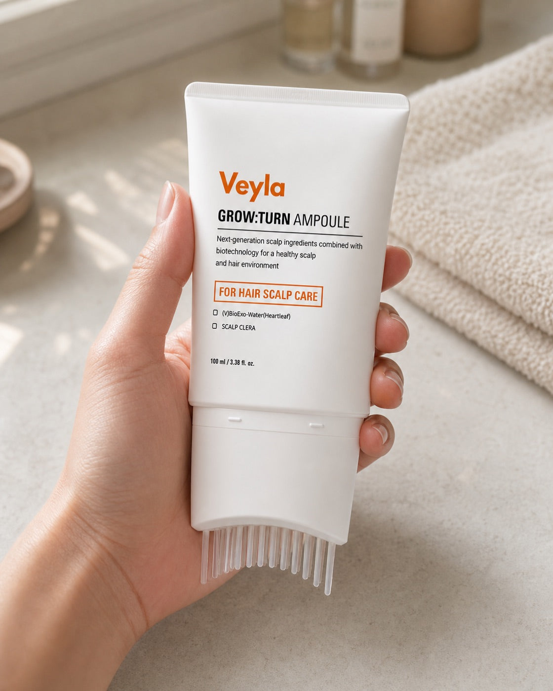 A hand holding the Veyla ampoule brush head down on a sunlit bathroom counter