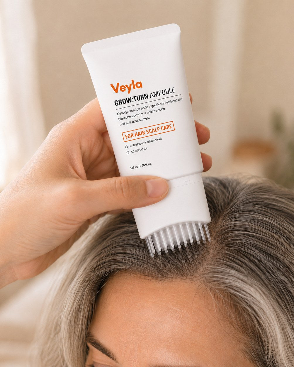 A hand pressing the Veyla ampoule brush onto the scalp along the part line